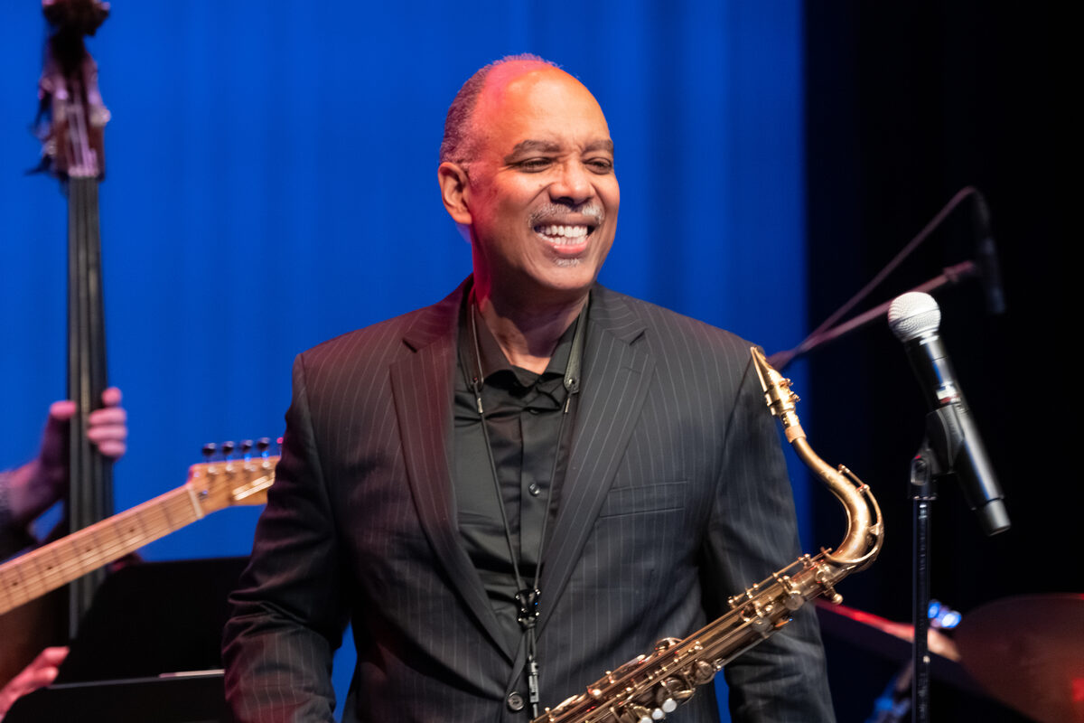 Don Braden performing on stage with his saxophone, smiling, in front of a blue backdrop